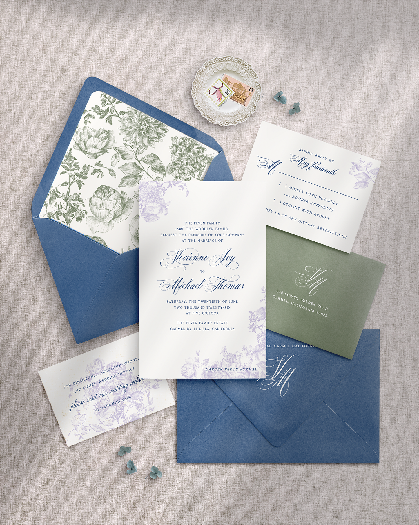 Wedding invitation set with floral and monogrammed elements on a gray surface