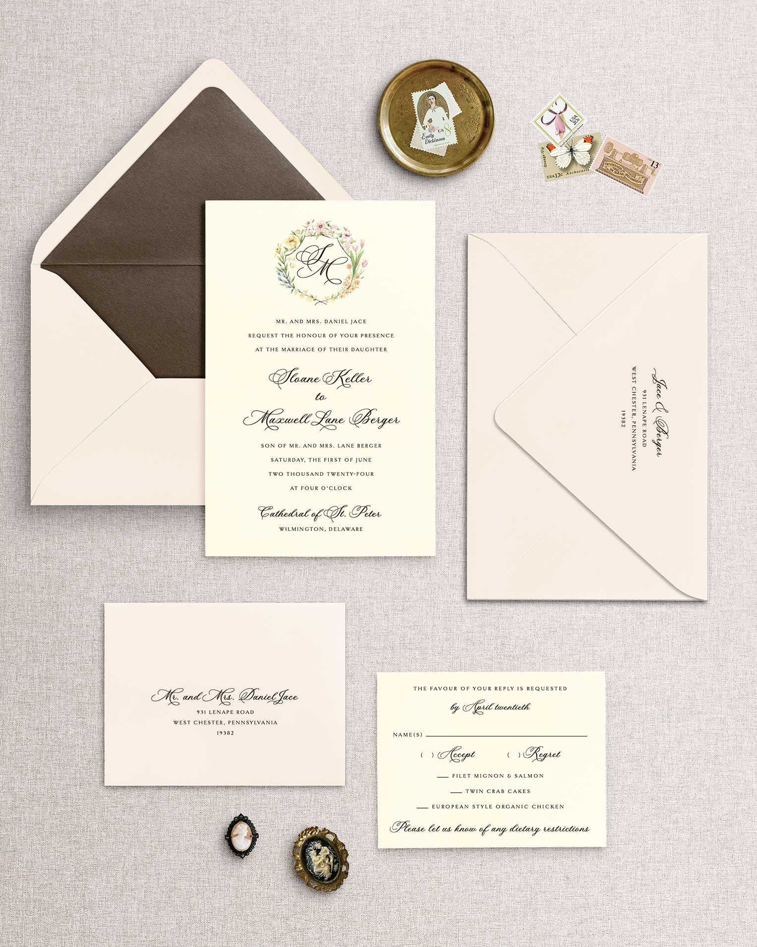 Collection of wedding invitations in blush and brown with a floral crest around a monogram on a textured surface