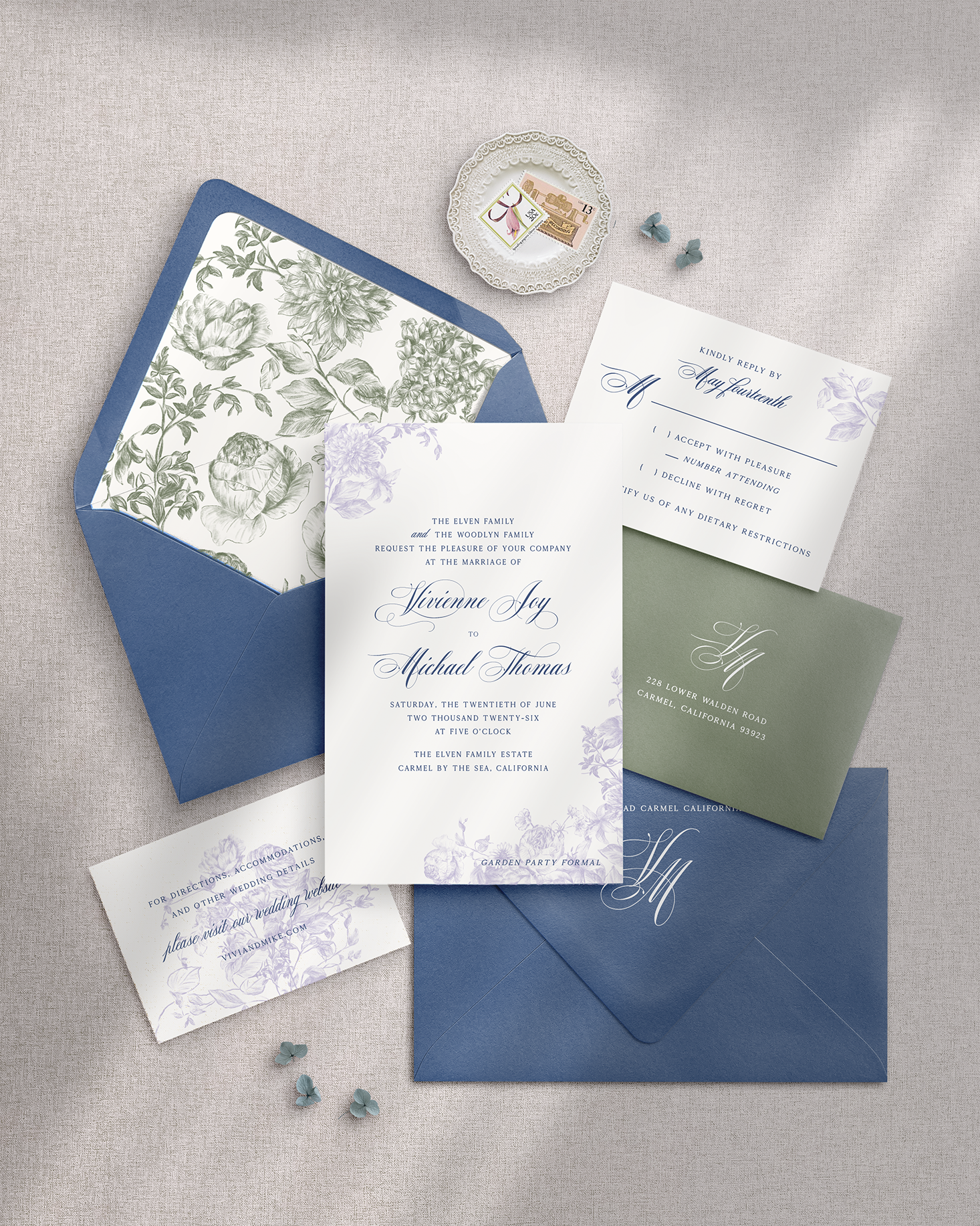 Wedding invitation set with floral and monogrammed elements on a gray surface